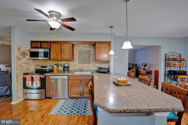 kitchen featuring appliances with stainless steel finishes, pendant lighting, sink, and light wood-type flooring