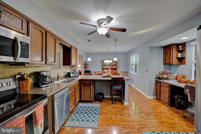 kitchen with light hardwood / wood-style floors, pendant lighting, sink, kitchen peninsula, and appliances with stainless steel finishes