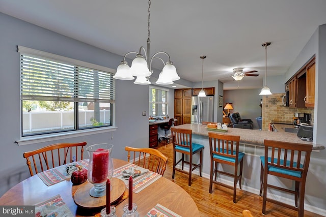 dining room with ceiling fan with notable chandelier and light hardwood / wood-style floors