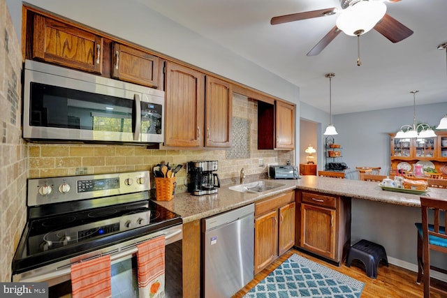 kitchen featuring light wood-type flooring, pendant lighting, tasteful backsplash, sink, and stainless steel appliances