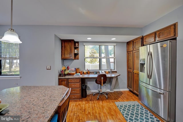 kitchen featuring light wood-type flooring, light stone counters, built in desk, stainless steel fridge, and pendant lighting