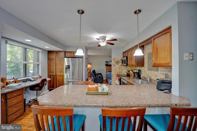 kitchen featuring ceiling fan, light hardwood / wood-style floors, kitchen peninsula, appliances with stainless steel finishes, and a kitchen bar