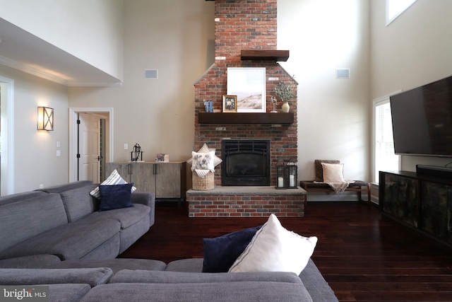 living room featuring crown molding, dark wood-type flooring, a high ceiling, and a brick fireplace