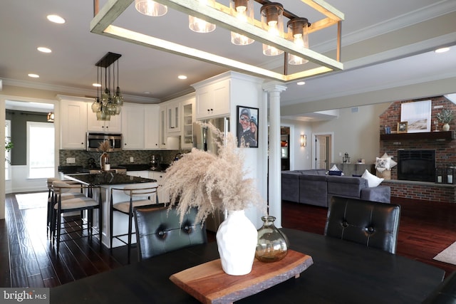 dining area with decorative columns, crown molding, dark wood-type flooring, and a brick fireplace