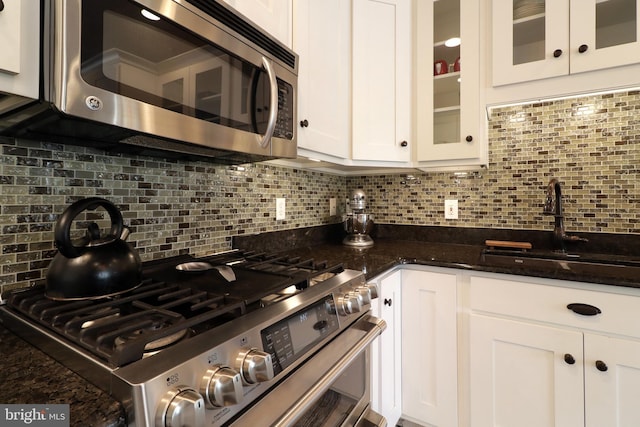 kitchen with dark stone countertops, white cabinetry, stainless steel appliances, and tasteful backsplash