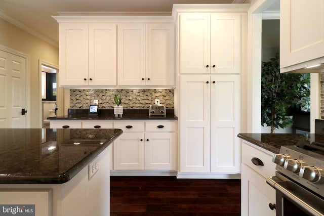 kitchen featuring backsplash, dark stone countertops, white cabinetry, and stainless steel range oven