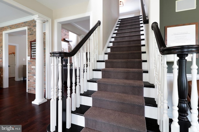 stairway featuring decorative columns, wood-type flooring, brick wall, and ornamental molding