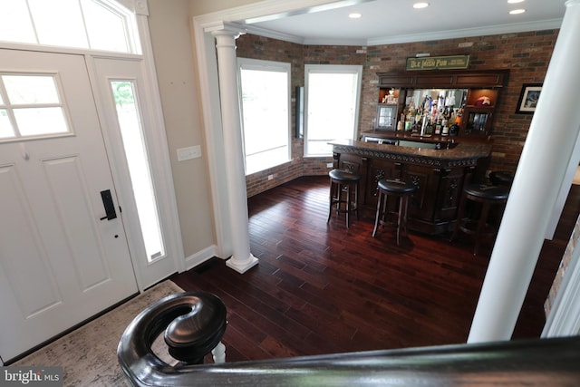 entryway featuring dark hardwood / wood-style floors, ornate columns, bar, and brick wall