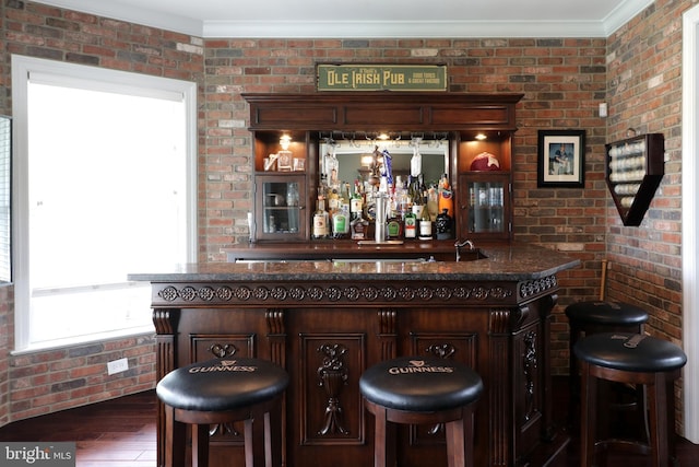 bar featuring dark brown cabinetry, ornamental molding, brick wall, and dark wood-type flooring