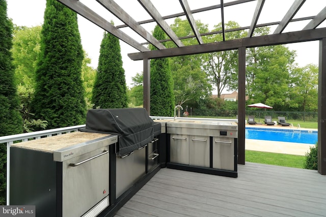 deck with an outdoor kitchen, a pergola, and a grill