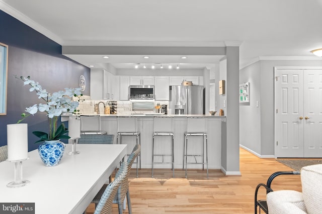 kitchen with stainless steel appliances, white cabinetry, a kitchen breakfast bar, light wood-type flooring, and kitchen peninsula