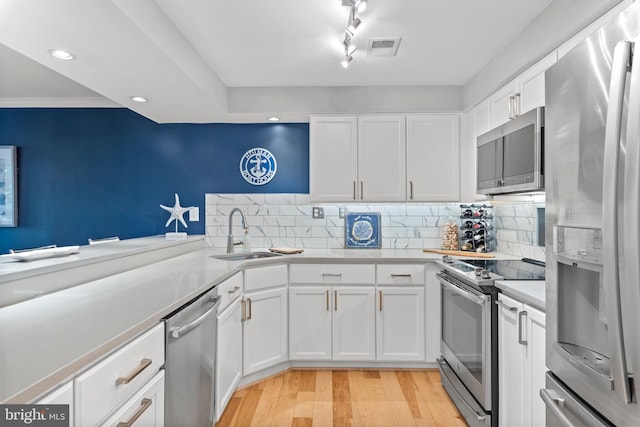 kitchen featuring sink, white cabinets, light wood-type flooring, tasteful backsplash, and appliances with stainless steel finishes