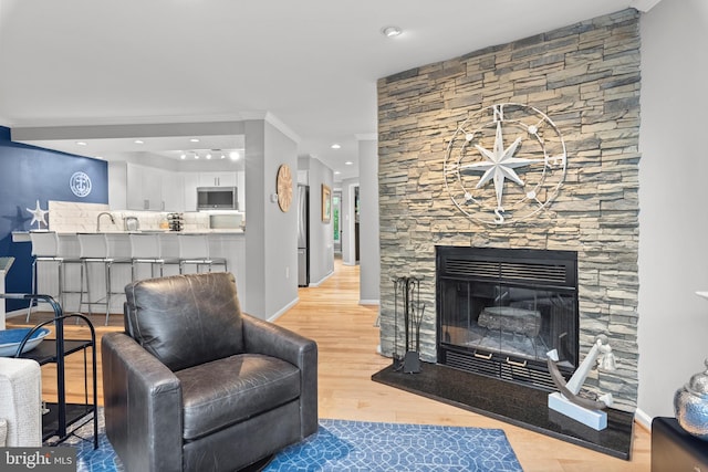 living room featuring sink, ornamental molding, light hardwood / wood-style flooring, and a stone fireplace