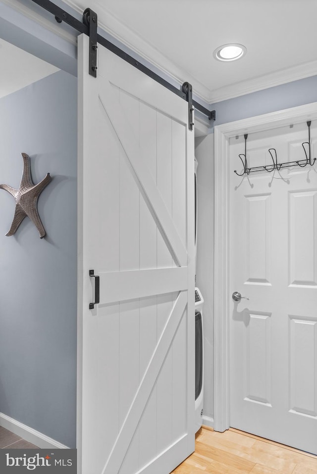 clothes washing area with ornamental molding, hardwood / wood-style floors, and a barn door