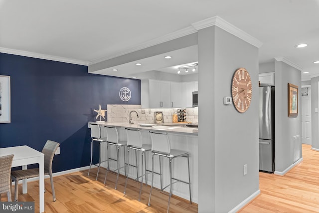 kitchen featuring light hardwood / wood-style flooring, stainless steel appliances, white cabinetry, and backsplash