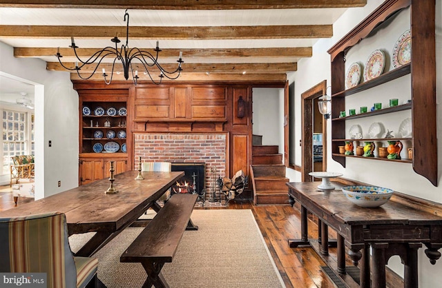 dining area featuring beam ceiling, a brick fireplace, dark wood-type flooring, and a notable chandelier