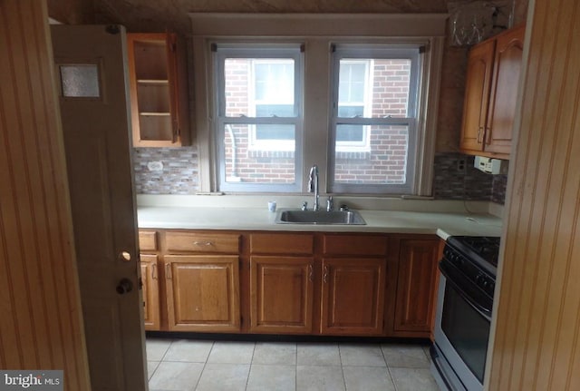 kitchen with light tile patterned floors, sink, black range oven, and tasteful backsplash