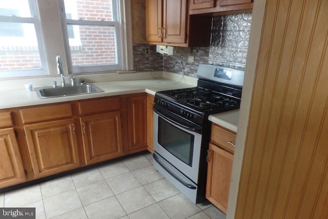 kitchen featuring backsplash, gas range, light tile patterned floors, and sink