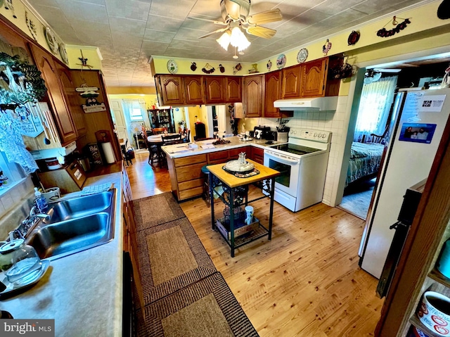 kitchen featuring kitchen peninsula, sink, white appliances, light hardwood / wood-style flooring, and backsplash