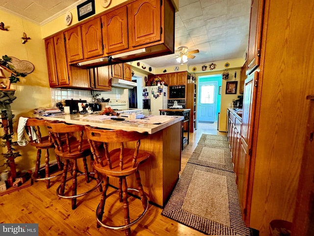 kitchen with a breakfast bar, kitchen peninsula, light hardwood / wood-style flooring, white appliances, and ornamental molding