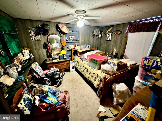 carpeted bedroom featuring wood walls and ceiling fan