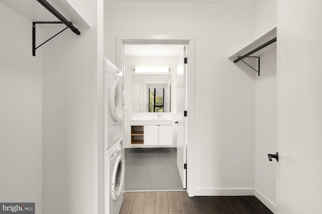 clothes washing area featuring stacked washer / drying machine, sink, and dark hardwood / wood-style flooring