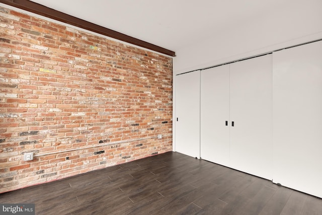 unfurnished bedroom featuring brick wall, a closet, and dark hardwood / wood-style floors