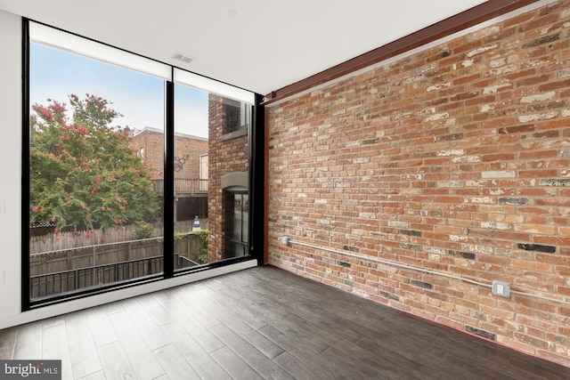 unfurnished room featuring brick wall, floor to ceiling windows, and hardwood / wood-style floors