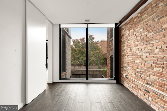 empty room with brick wall, a wall of windows, and dark wood-type flooring