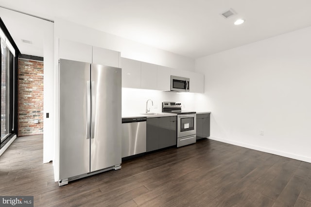 kitchen featuring appliances with stainless steel finishes, brick wall, white cabinets, dark hardwood / wood-style flooring, and sink