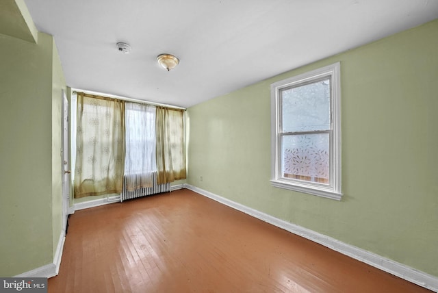 unfurnished room featuring wood-type flooring and a baseboard heating unit