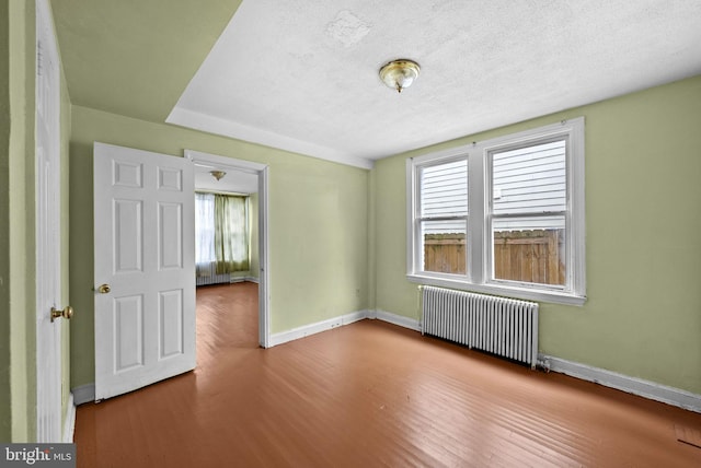 spare room with wood-type flooring, radiator heating unit, and a textured ceiling