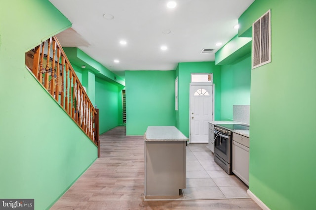 kitchen with a kitchen island, white cabinetry, stainless steel range with electric cooktop, light stone countertops, and light hardwood / wood-style floors