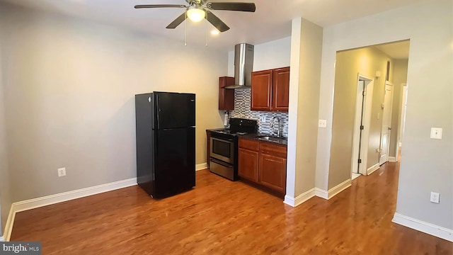 kitchen with electric range, sink, wall chimney exhaust hood, backsplash, and black refrigerator