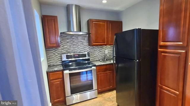 kitchen featuring stone counters, stainless steel range, wall chimney exhaust hood, tasteful backsplash, and black fridge