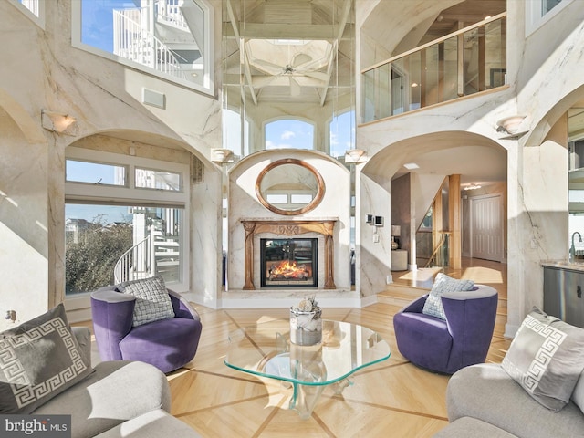 living room featuring a premium fireplace, ceiling fan, and a towering ceiling