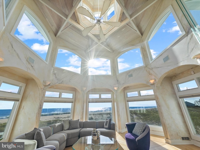 living room featuring ceiling fan, light hardwood / wood-style floors, a towering ceiling, and a healthy amount of sunlight