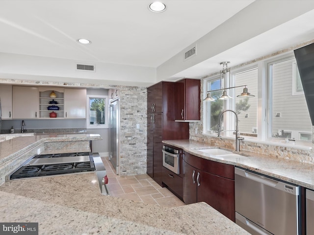 kitchen with light stone counters, pendant lighting, appliances with stainless steel finishes, and sink