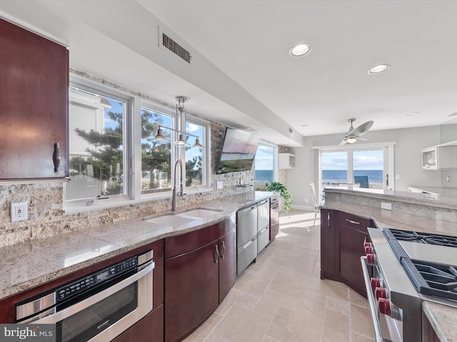 kitchen with light stone countertops, stainless steel appliances, sink, decorative light fixtures, and backsplash