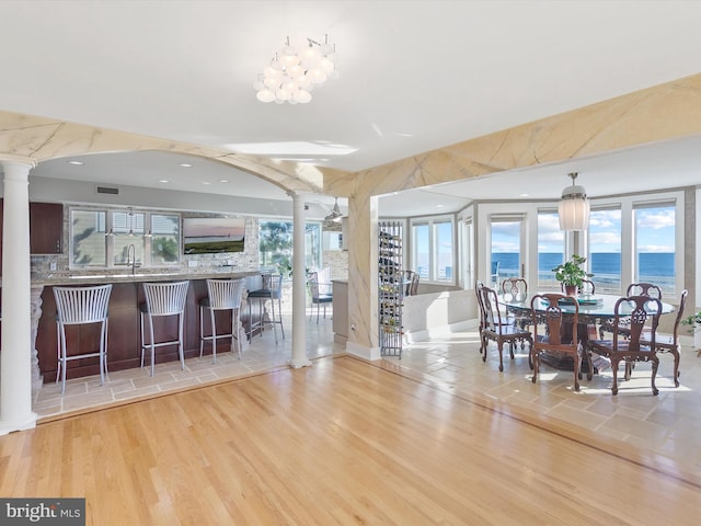 kitchen featuring light hardwood / wood-style floors, ornate columns, a breakfast bar, sink, and backsplash