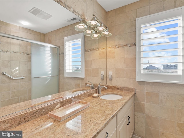 bathroom with a shower with shower door, vanity, and tile walls