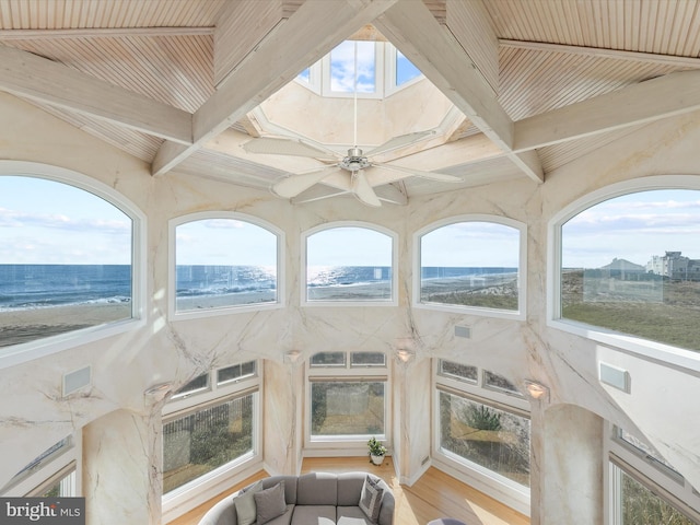 unfurnished sunroom featuring a water view, a view of the beach, beam ceiling, and plenty of natural light