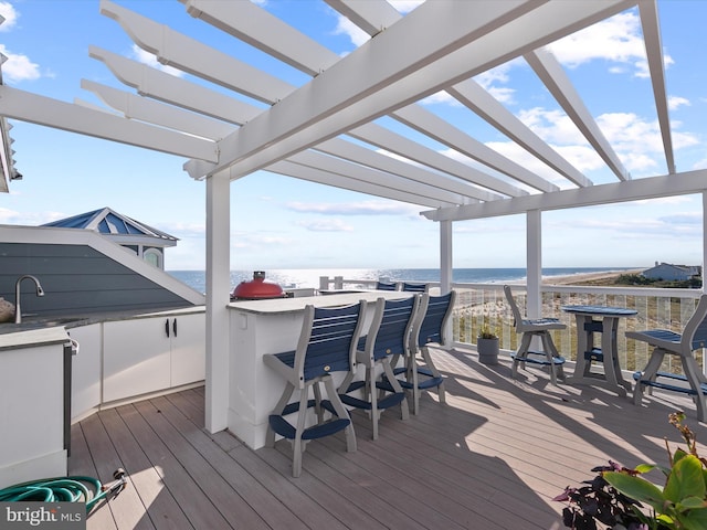 deck with a water view, a beach view, a wet bar, and a pergola