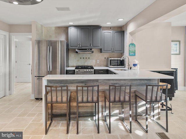 kitchen featuring sink, kitchen peninsula, appliances with stainless steel finishes, a breakfast bar area, and decorative backsplash