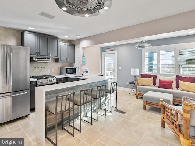 kitchen with sink, gray cabinetry, backsplash, appliances with stainless steel finishes, and a breakfast bar area