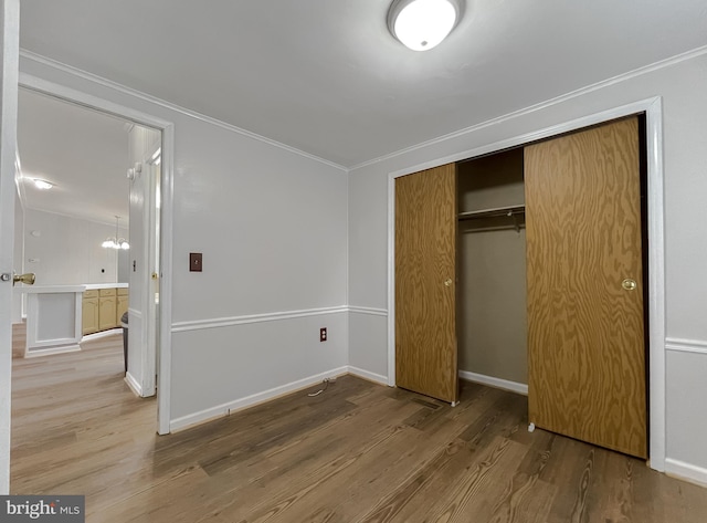 unfurnished bedroom with an inviting chandelier, ornamental molding, a closet, and light wood-type flooring