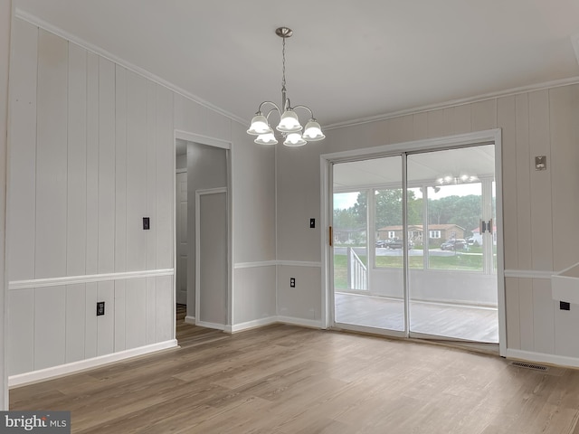 unfurnished dining area with wood walls, ornamental molding, an inviting chandelier, and hardwood / wood-style floors