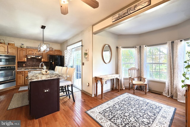 kitchen featuring light stone counters, black fridge, an island with sink, pendant lighting, and hardwood / wood-style flooring