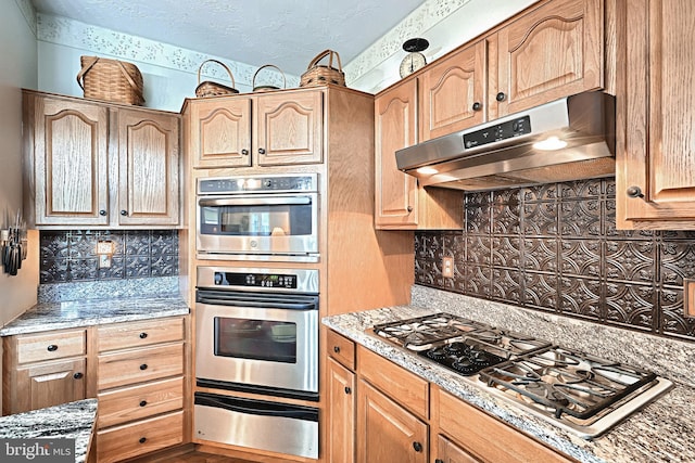 kitchen featuring appliances with stainless steel finishes, stone countertops, decorative backsplash, and a textured ceiling