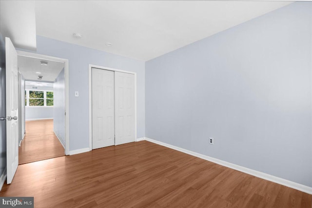 unfurnished bedroom with wood finished floors, baseboards, and a closet